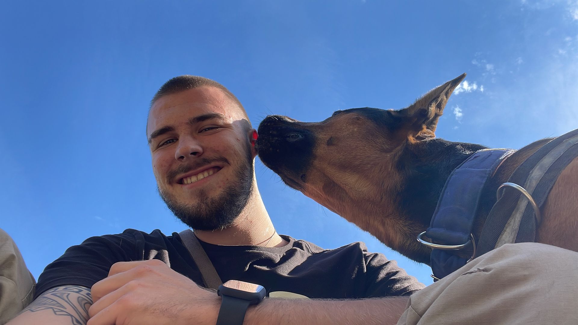 Hundetrainer Leon Weisbecker lächelt in die Kamera, während ihm sein Hund über die Wange schleckt